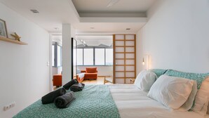 A modern hotel room with a large bed, a sofa, and a view of the city. - Sunset Bliss - Breathtaking Beach Apartment (Almada)