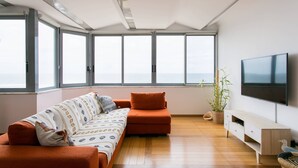 A modern living room with a sofa, a TV, and large windows offering a view of the sea. - Sunset Bliss - Breathtaking Beach Apartment (Almada)