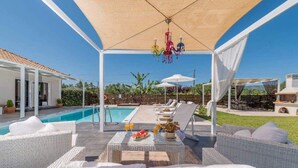 Zona de piscina exterior cubierta con sillones de relax y una mesa lista para el desayuno.