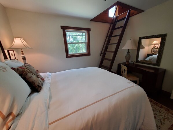A bedroom with a bed, a window, a ladder, a desk, and a mirror.