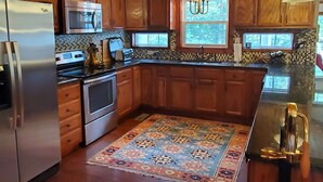 Une cuisine avec des meubles en bois, des appareils électroménagers en acier inoxydable, un tapis à motifs et un lustre.