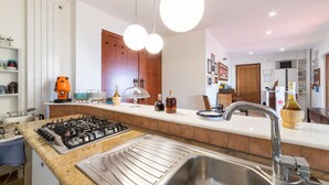 Une cuisine moderne équipée d’une cuisinière à gaz, d’un évier en acier inoxydable et de luminaires suspendus.