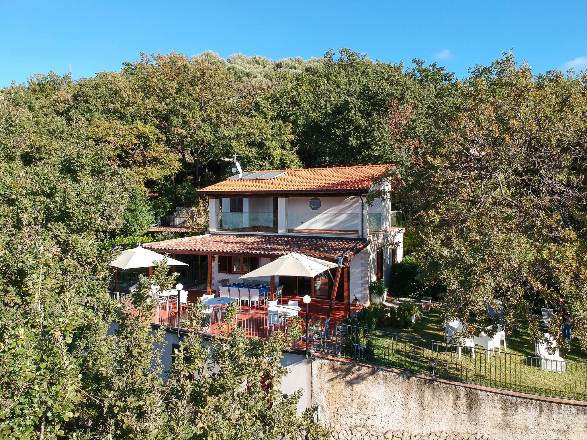 A two-story house with a tiled roof, surrounded by trees.