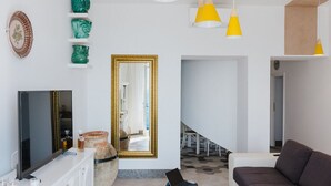 A modern living room with a flat-screen TV, a sofa, and a coffee table. There are yellow pendant lights and a large mirror on the wall.