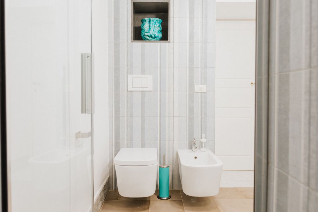 Un baño con inodoro, bidé y un pequeño estante con un objeto decorativo.