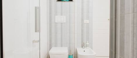 Un baño con inodoro, bidé y un pequeño estante con un objeto decorativo.