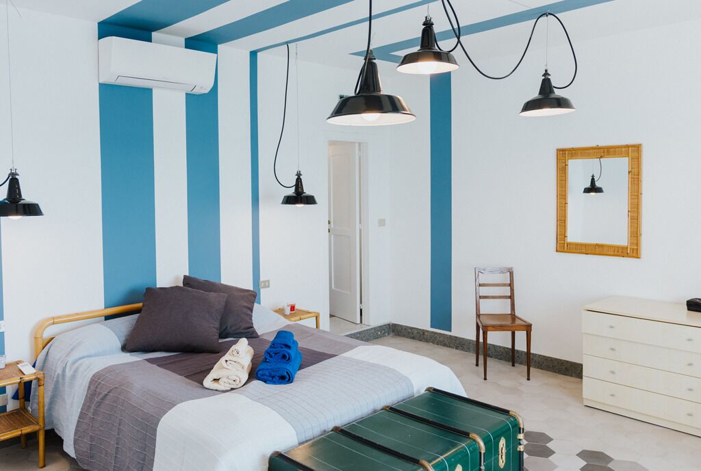 Een slaapkamer met een bed, nachtkastje, lamp, stoel, kapstok en een spiegel aan de muur.