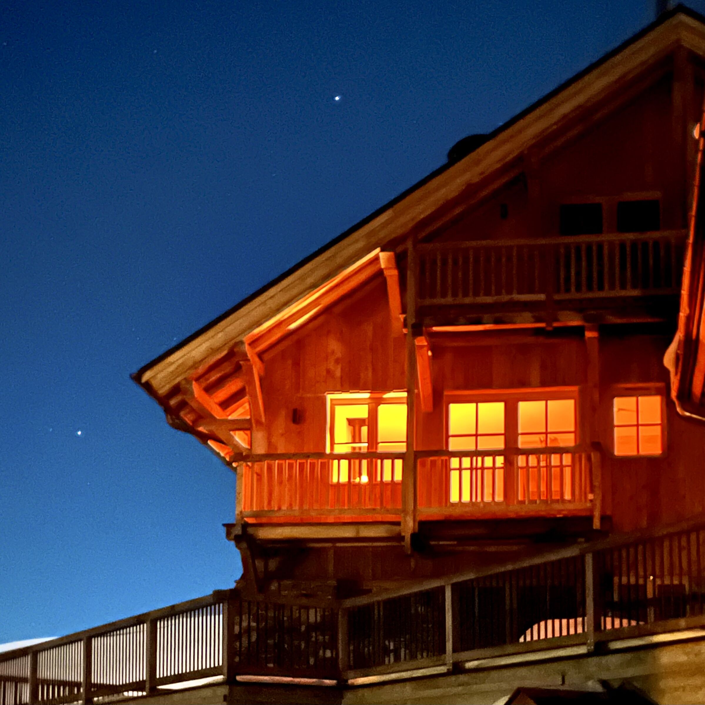 Een tweelaags houten gebouw met een balkon en meerdere ramen, verlicht in de nacht.