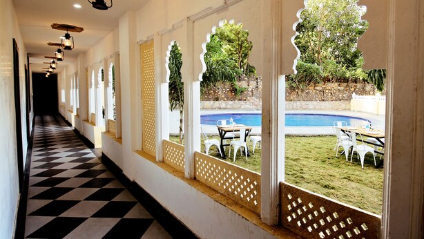 A corridor with a checkered floor leading to a pool area with outdoor seating. - The Kanchangarh Resort (Udaipur)