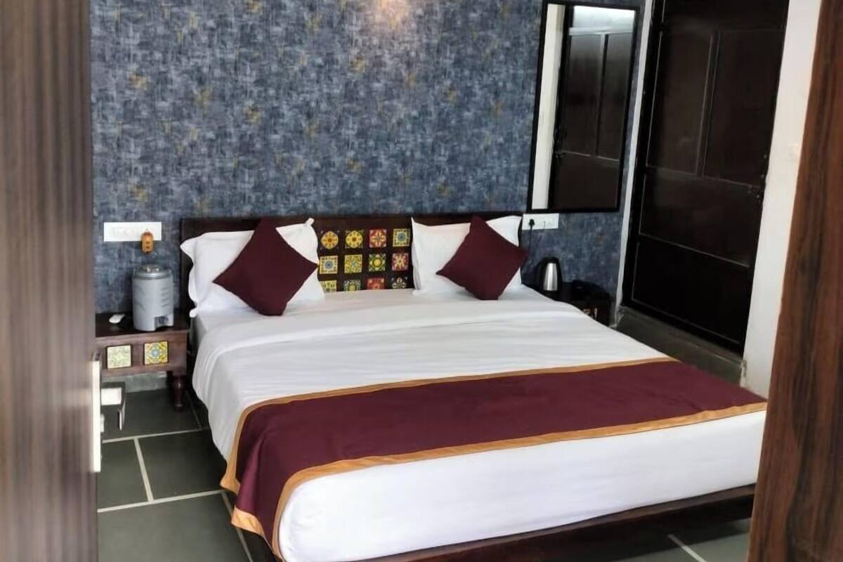 A hotel room with a large bed, a nightstand, a wall-mounted lamp, and a red rug.