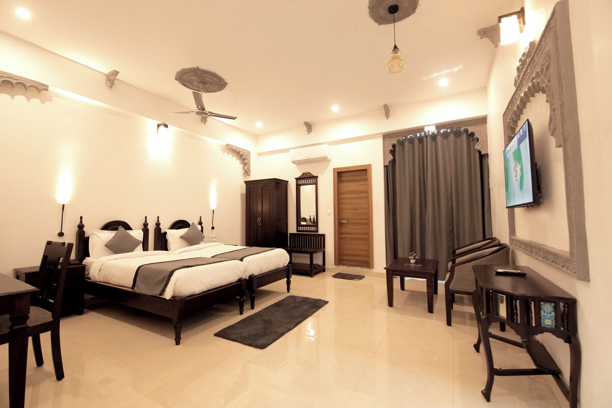 A well-lit bedroom with a double bed, bedside tables, a desk, and a TV.