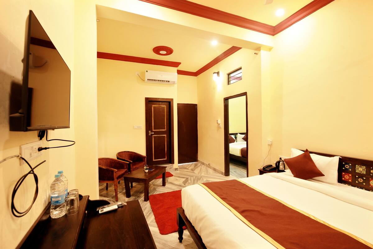 A hotel room with a bed, a desk, a chair, a TV, and an air conditioning unit.