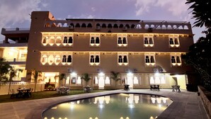 A traditional building with arched windows and a pool in the foreground. - The Kanchangarh Resort (Udaipur)