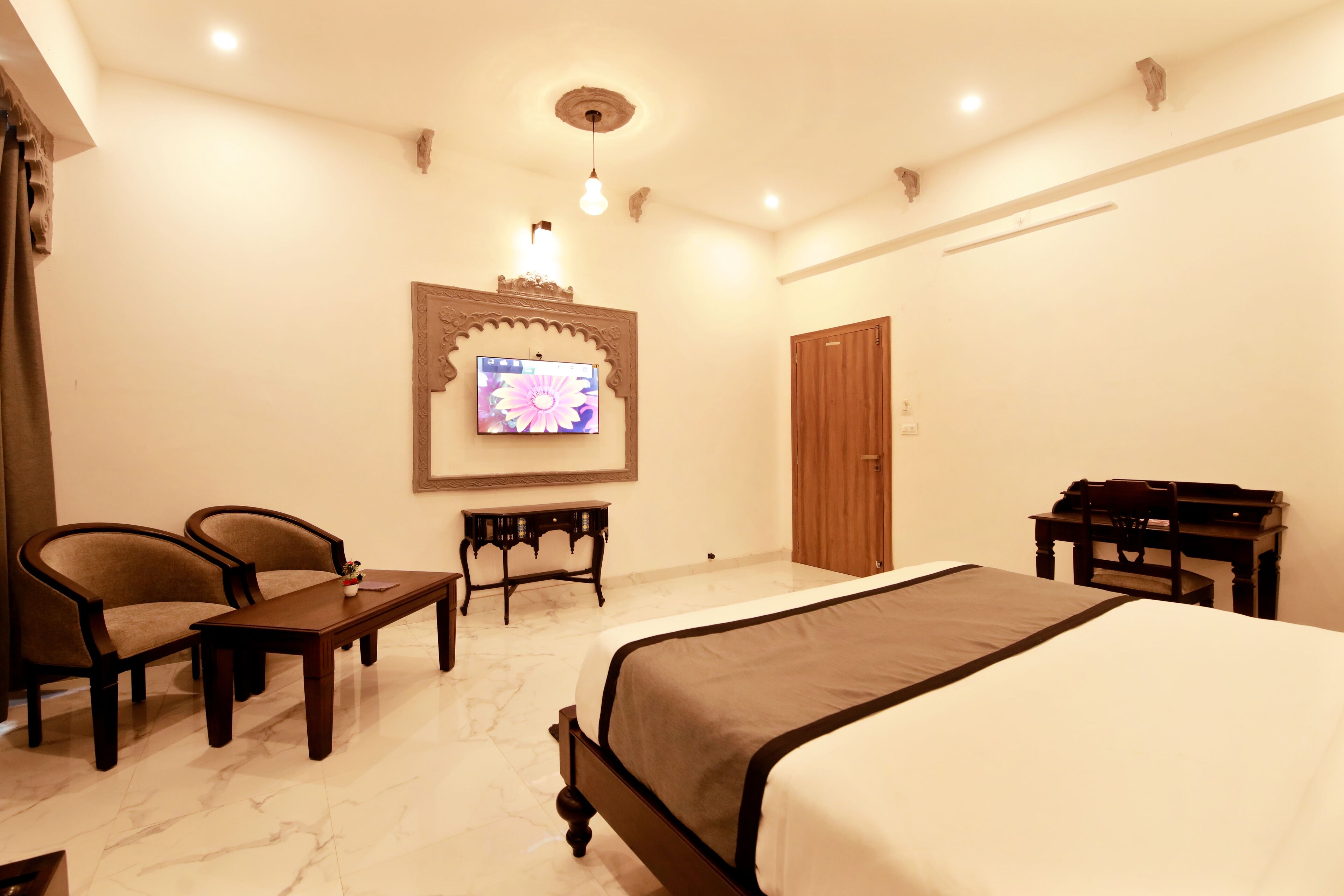 Una habitación de hotel con una cama, dos sillones, una mesita, televisor y un escritorio de madera.