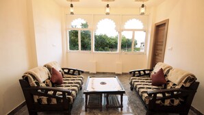 A room with two sofas, a table, and a window with a view of greenery. - The Kanchangarh Resort (Udaipur)