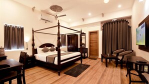 A spacious bedroom with a four-poster bed, a ceiling fan, a flat-screen TV, and a seating area with a table and chairs. - The Kanchangarh Resort (Udaipur)