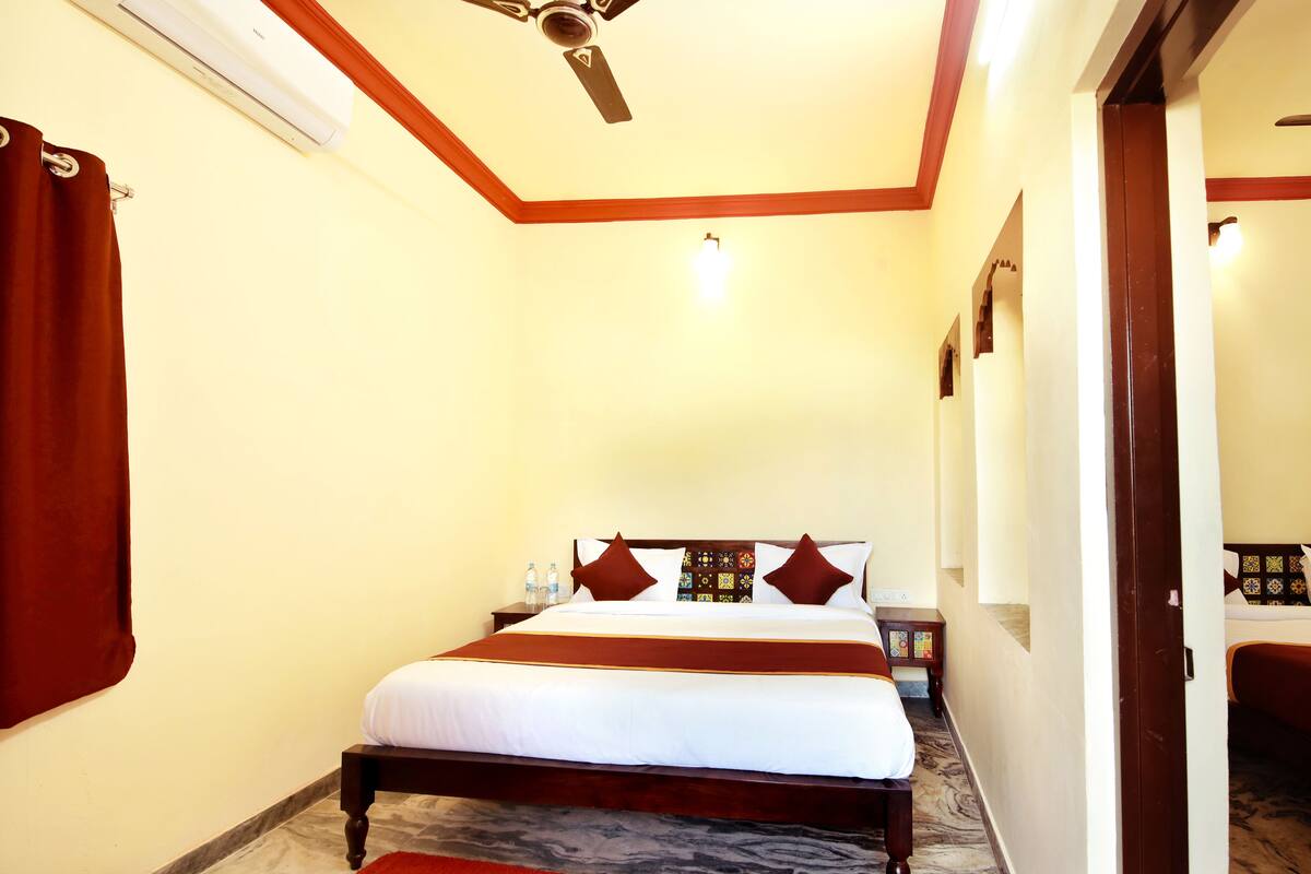 A hotel room with a bed, a ceiling fan, a nightstand, and a bathroom visible through an open door.