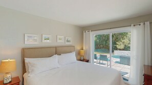 A hotel room with a bed, a nightstand with a lamp, a window with curtains, and framed pictures on the wall.