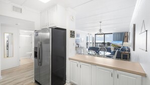 Una cucina moderna con mobili bianchi, un frigorifero in acciaio inossidabile e vista all'esterno tramite un'ampia finestra.