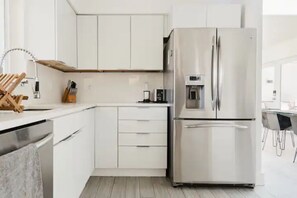 Une cuisine moderne avec des meubles blancs, un réfrigérateur en acier inoxydable et une machine à café intégrée.