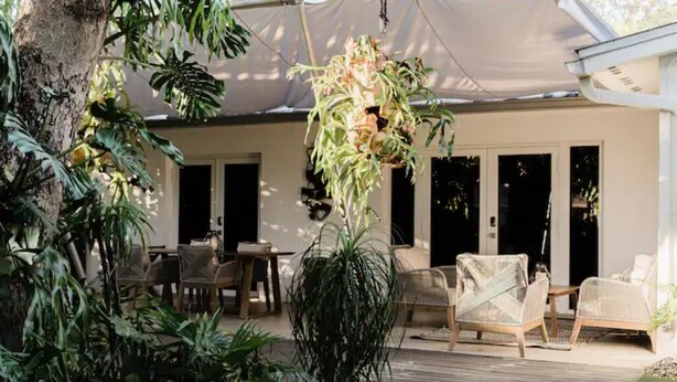 An outdoor patio with wicker furniture, a hanging plant, and a wooden deck. - Modern  Relaxing Zen ~ 5 ★  New pool, HotTub, Magic Garden!  (Wilton Manors)