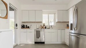 A modern kitchen with white cabinets, stainless steel appliances, and a window providing natural light. - Modern  Relaxing Zen ~ 5 ★  New pool, HotTub, Magic Garden!  (Wilton Manors)