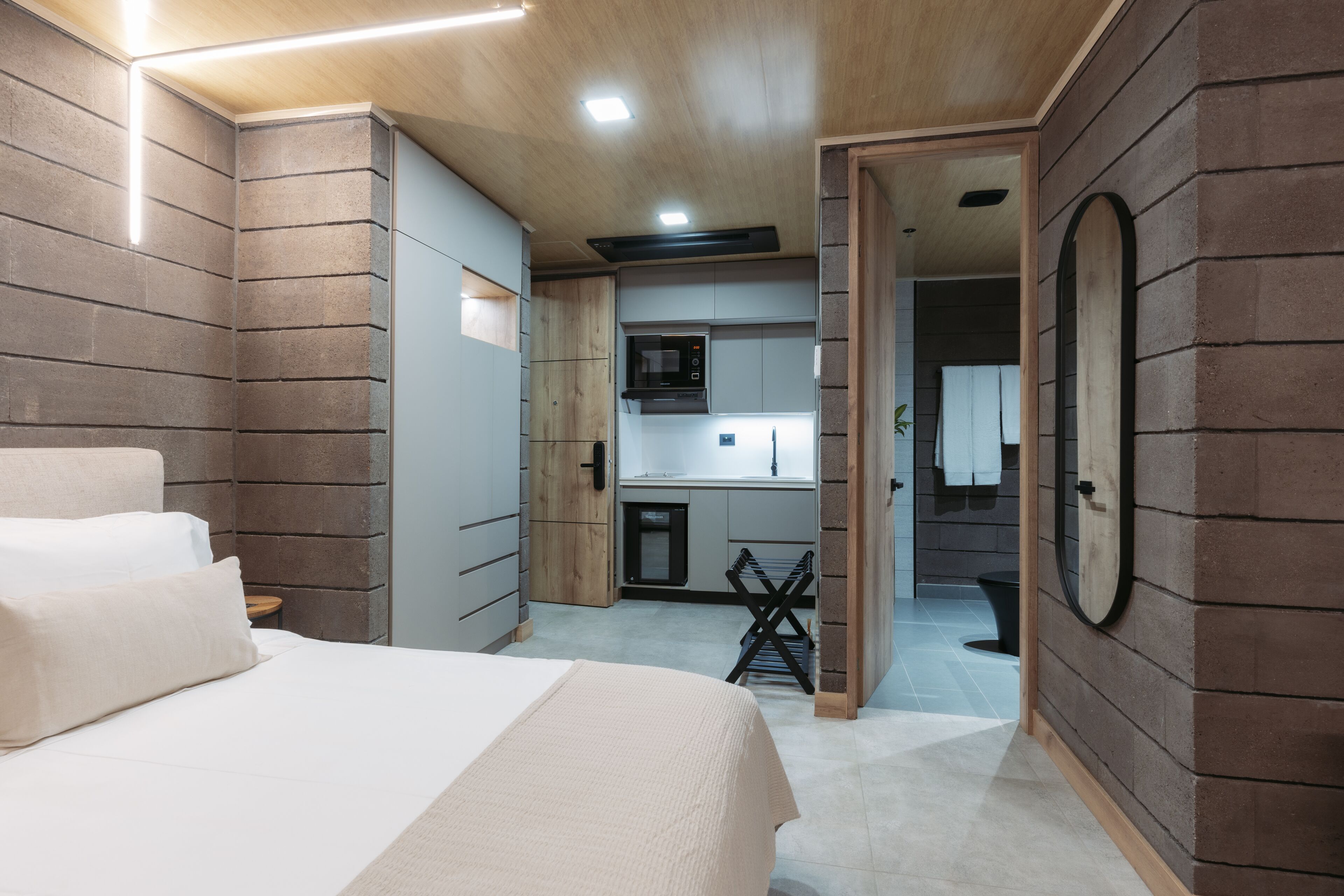 A modern bedroom with a bed, a small desk, and a bathroom visible through an open door.