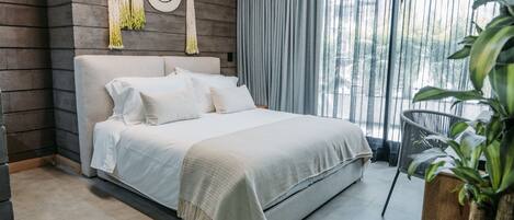 Un dormitorio moderno con una cama grande, un cabecero de madera, un colgador de macramé en la pared y vistas a zonas verdes a través de una ventana.