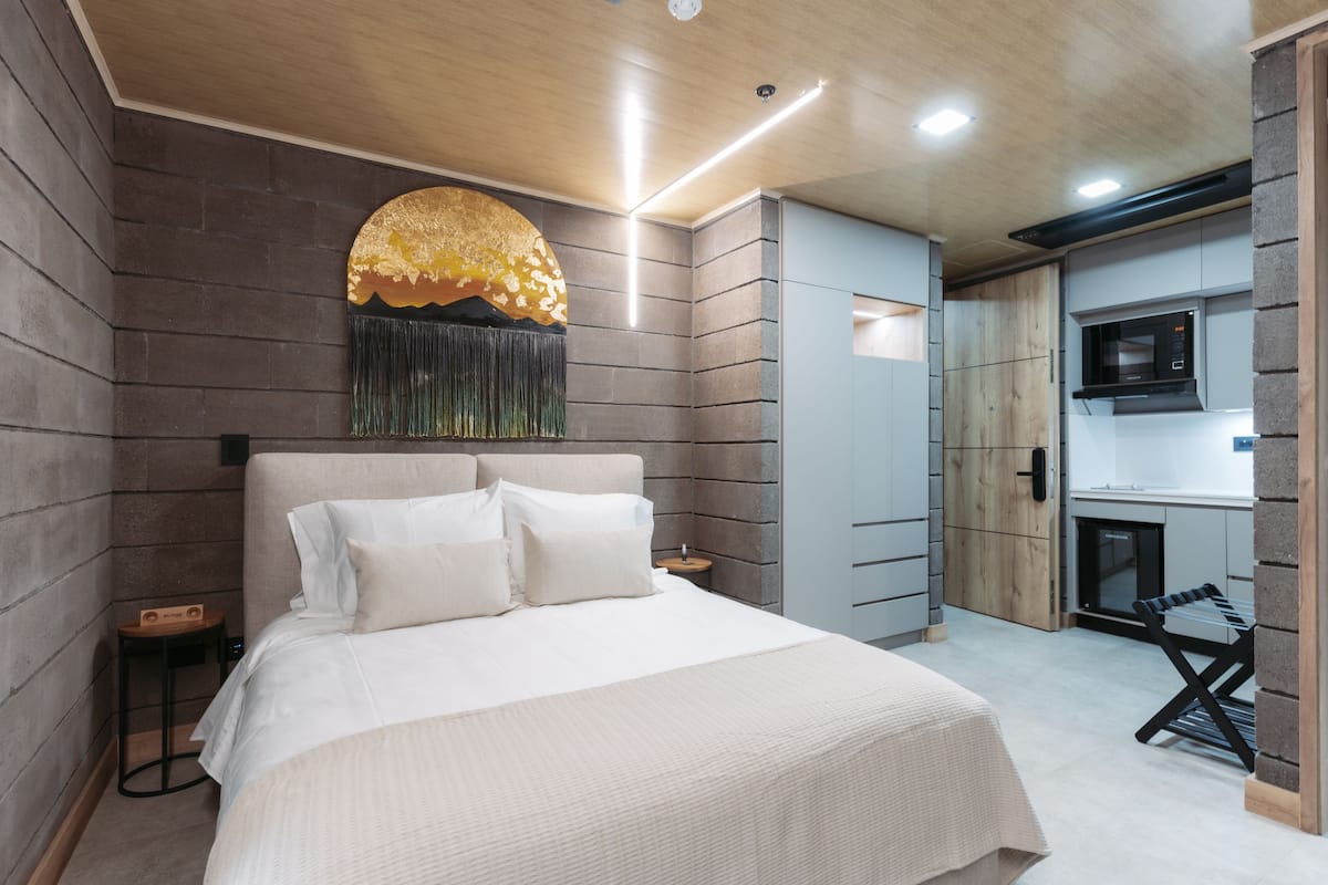 Een moderne slaapkamer met een groot bed, een klein nachtkastje, een aan de muur bevestigde televisie en een kitchenette.