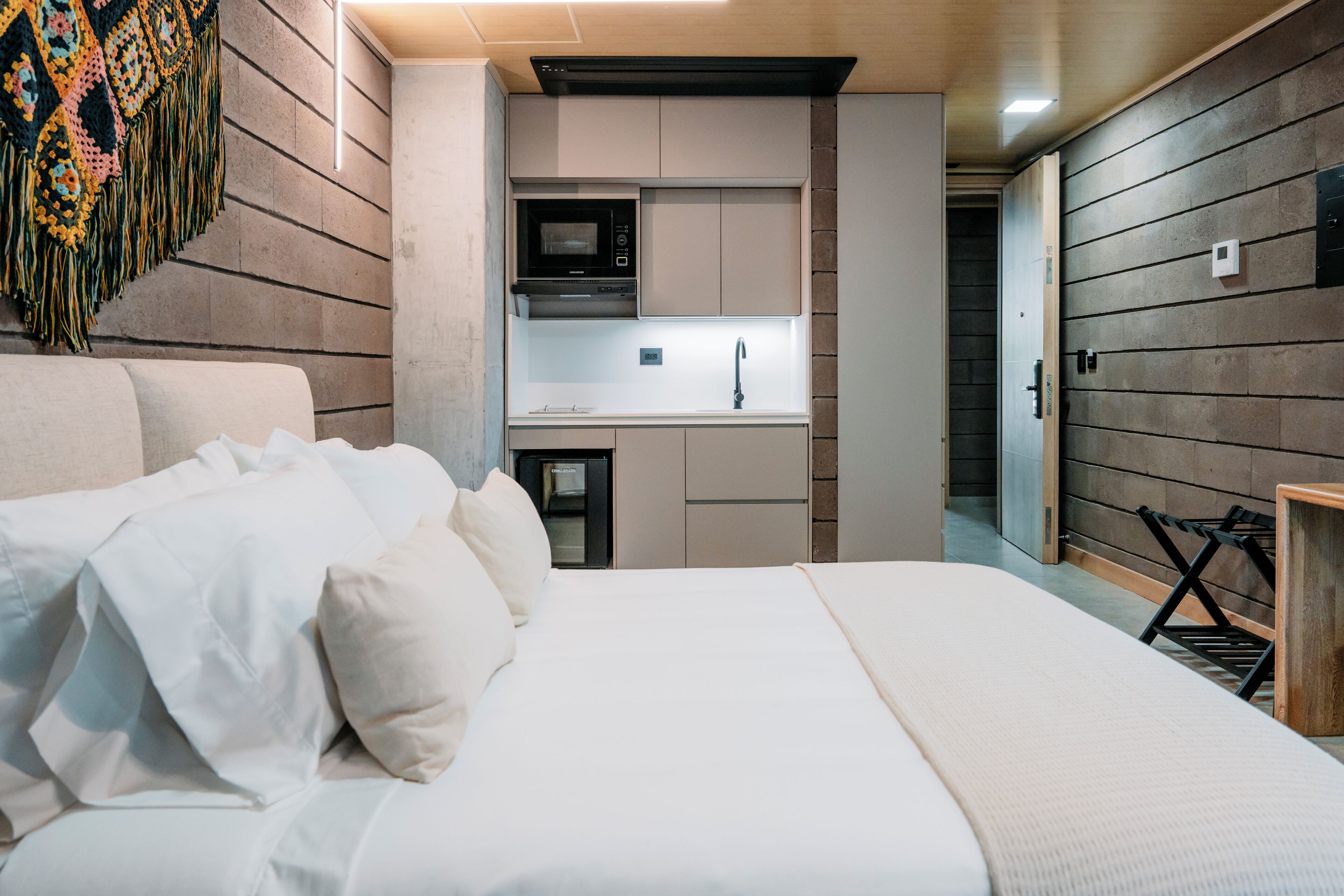 A modern hotel room with a large bed, a kitchenette, and a small bathroom.