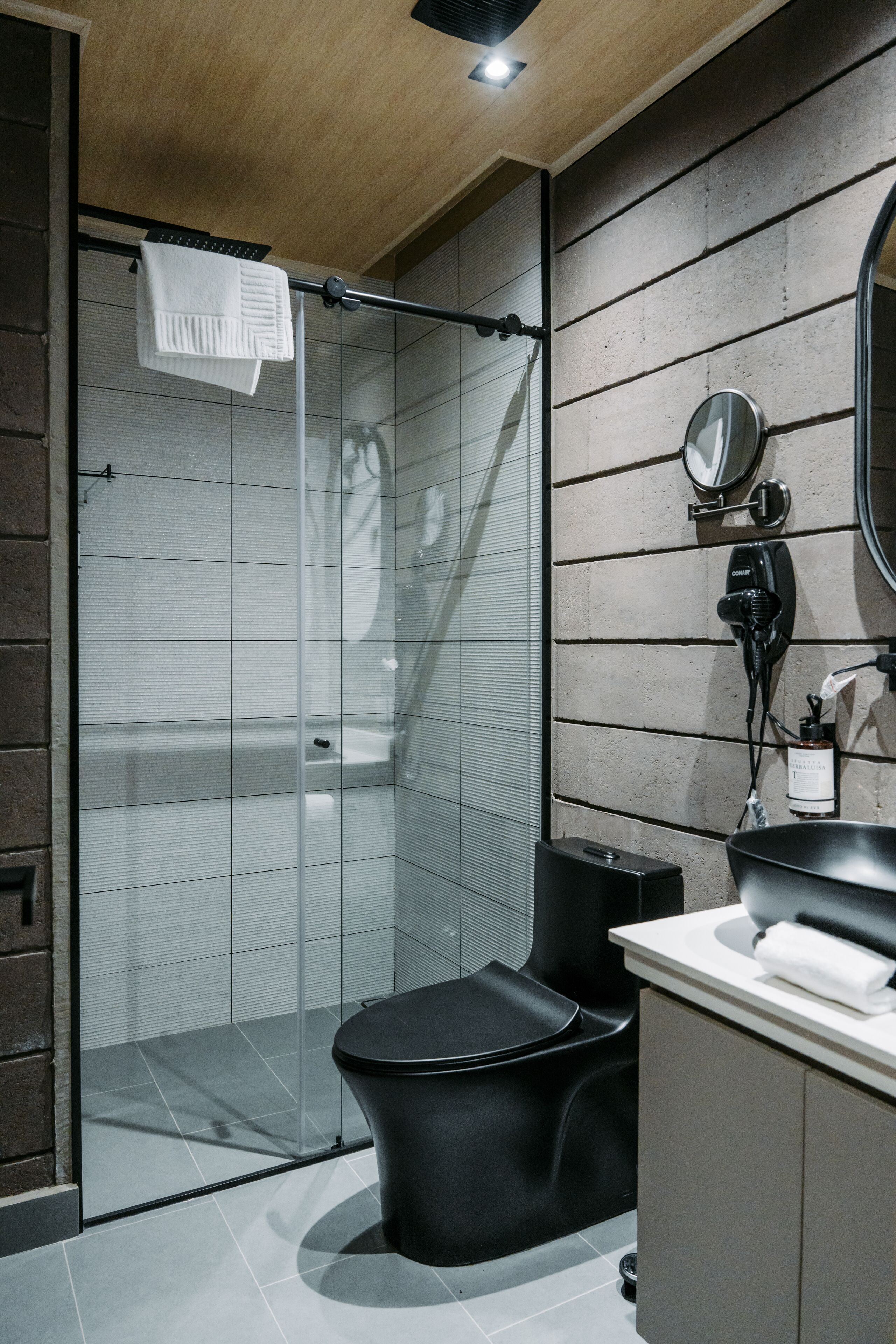 A modern bathroom with a glass shower enclosure, a black toilet, and a vanity with a mirror.