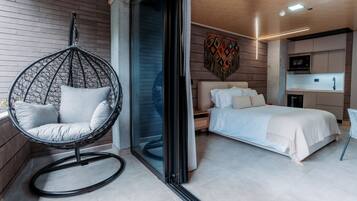 A modern bedroom with a hanging chair, a bed, and a kitchenette.