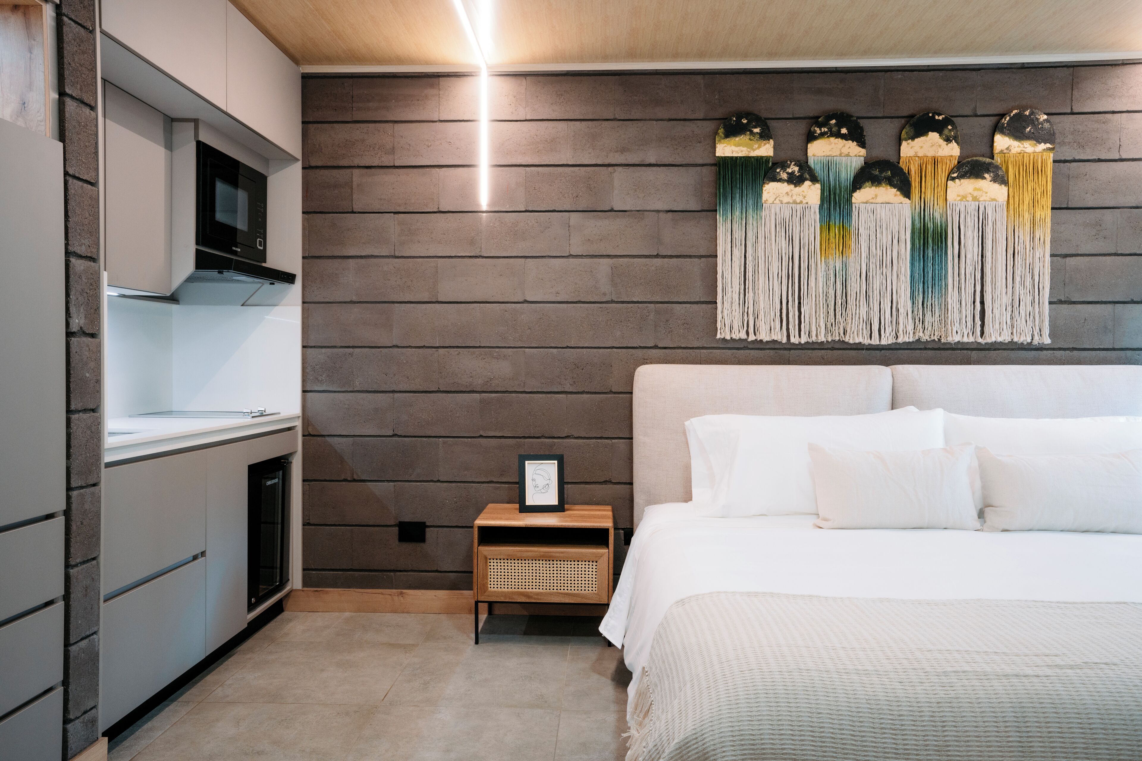 A modern bedroom with a bed, a nightstand, a microwave, and a wall-mounted decorative piece.