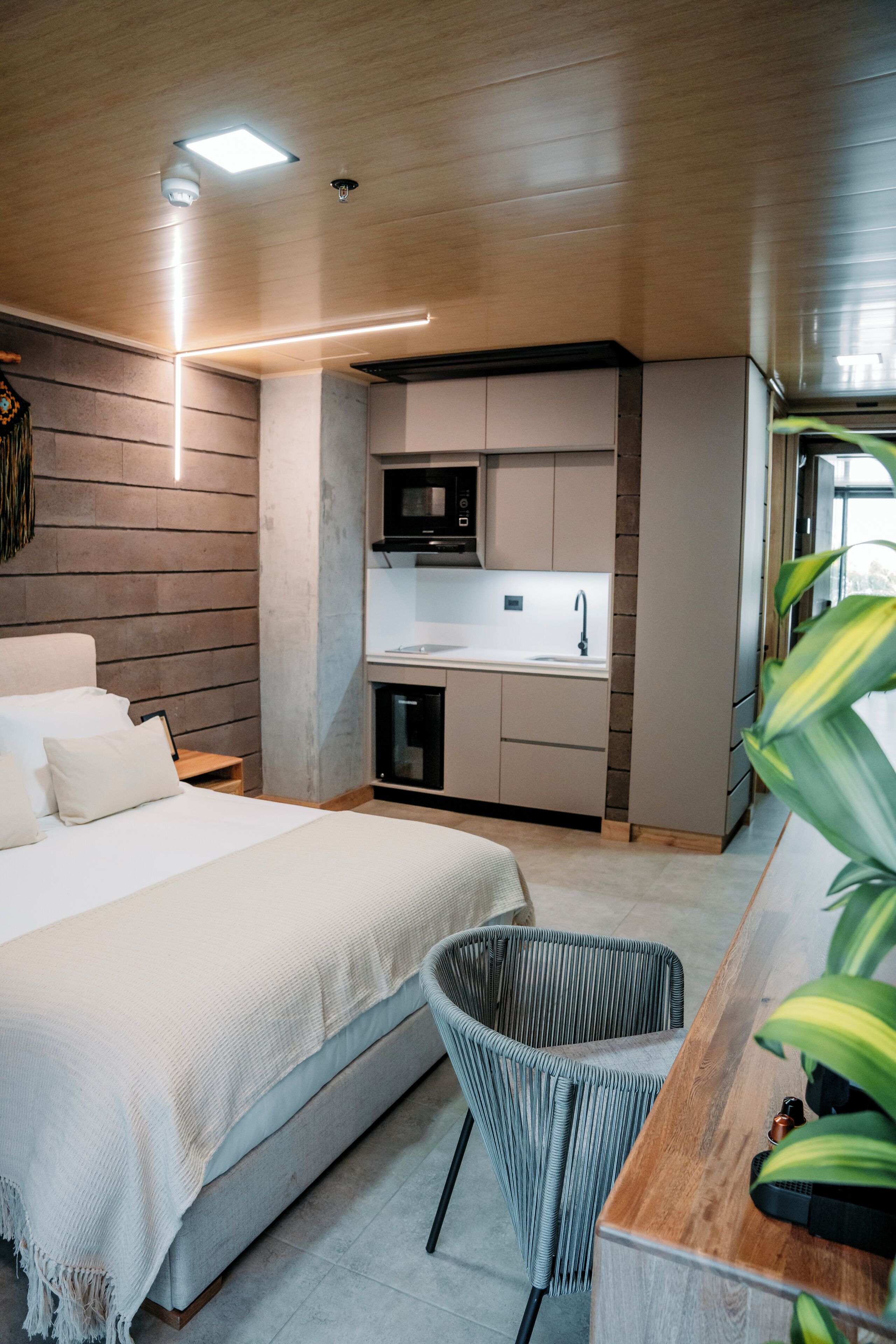 A modern bedroom with a large bed, a small kitchenette, and a dining area with a chair and table.