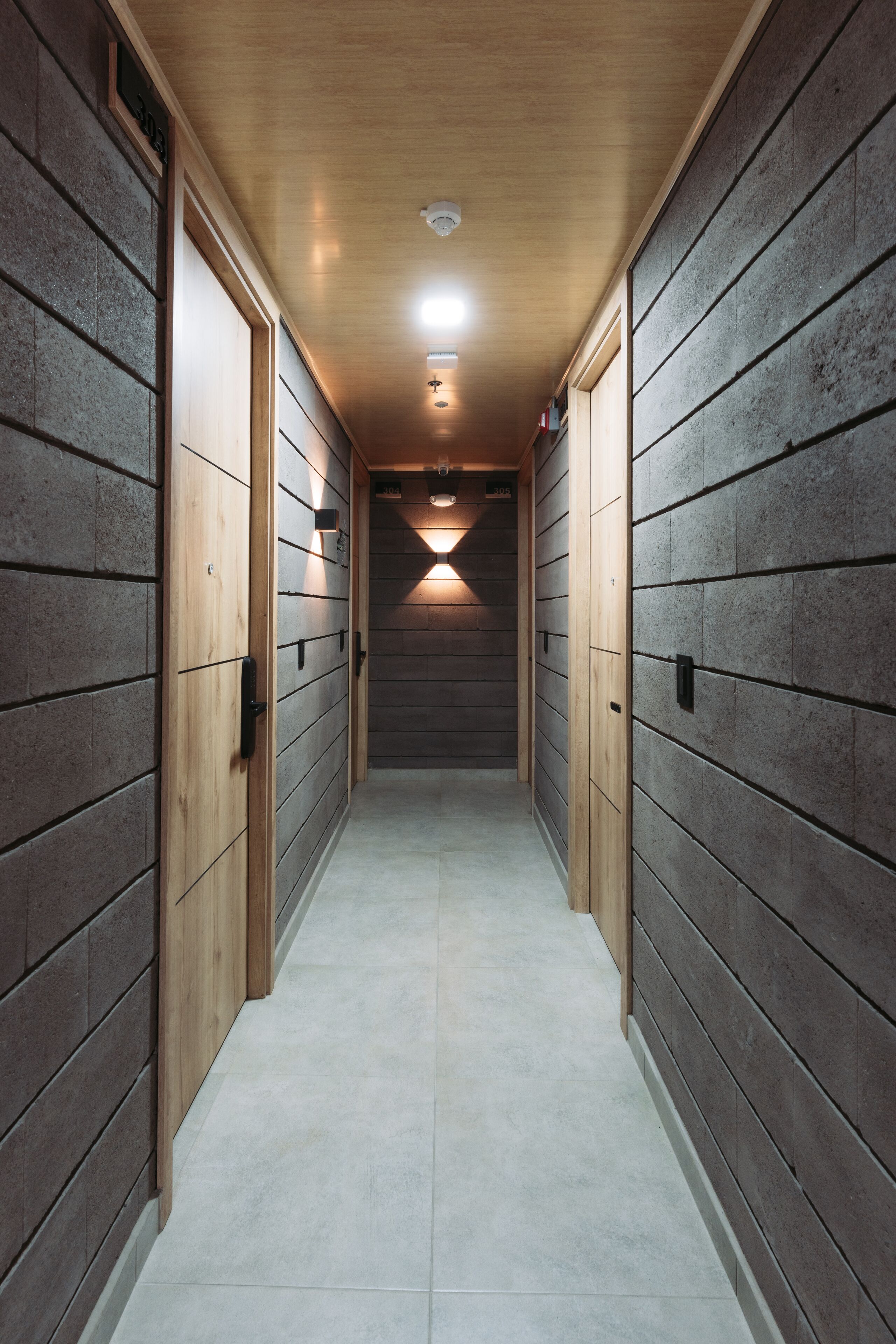 A narrow hallway with wooden walls and doors, leading to a lit area at the end.