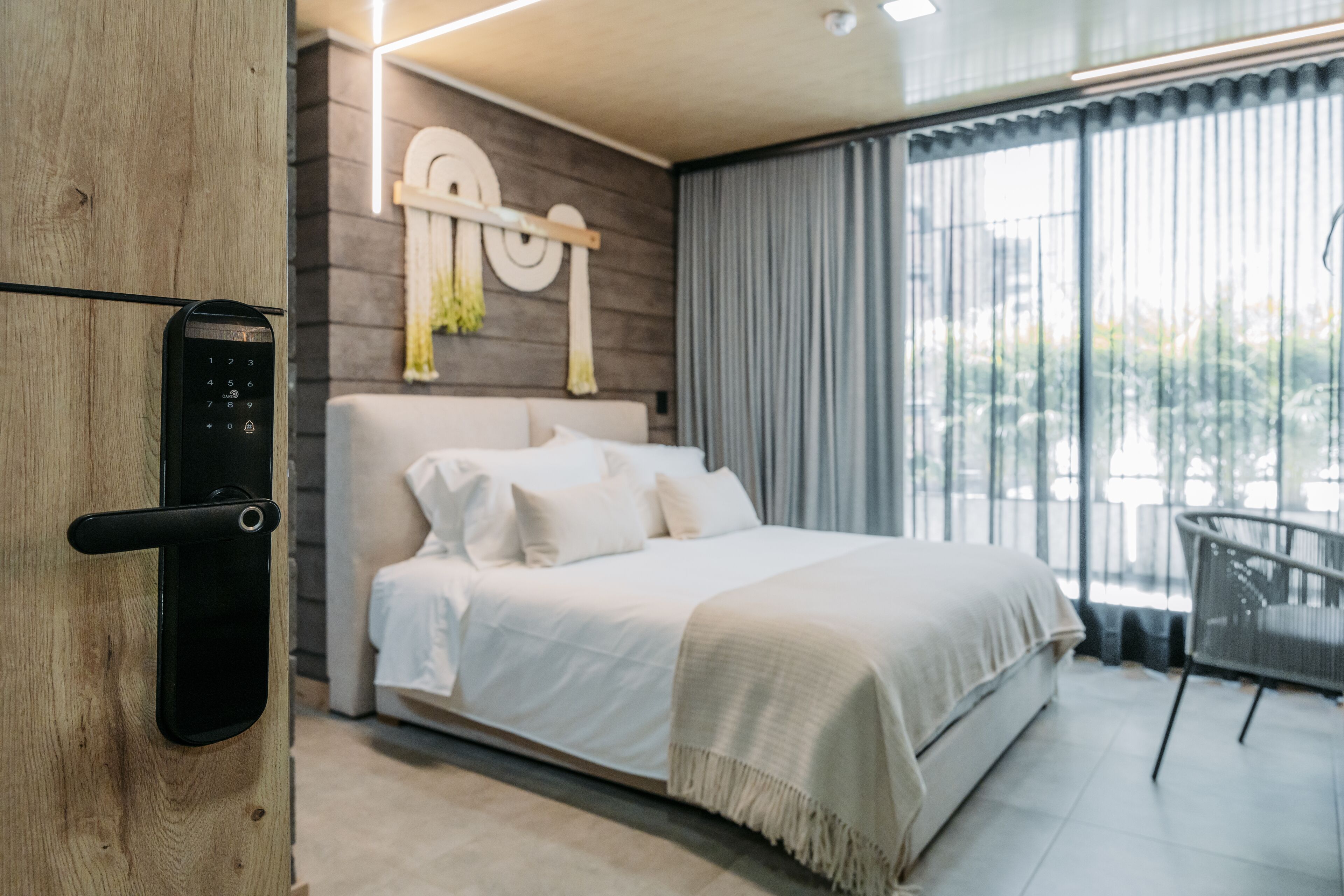 Une chambre moderne avec un lit, une serrure numérique, un luminaire fixé au mur et une vue par la fenêtre.