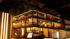 Uma área de bar com várias prateleiras de garrafas, um balcão com um computador e um refrigerador.