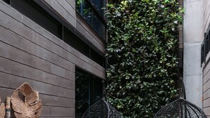 Um espaço moderno ao ar livre com parede de jardim vertical, móveis de vime e cadeiras suspensas.