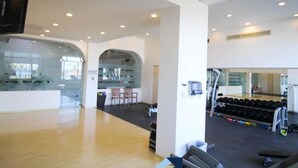 A spacious gym with a wooden floor, weightlifting equipment, and a mirrored wall. - Departamentos CB1 (Mazatlán)