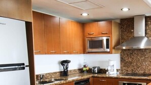 A modern kitchen with wooden cabinets, a stainless steel microwave, and granite countertops. - Departamentos CB1 (Mazatlán)