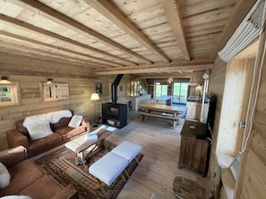 Interior de una cabaña de troncos con sofá, banca, mesa y estufa de leña.