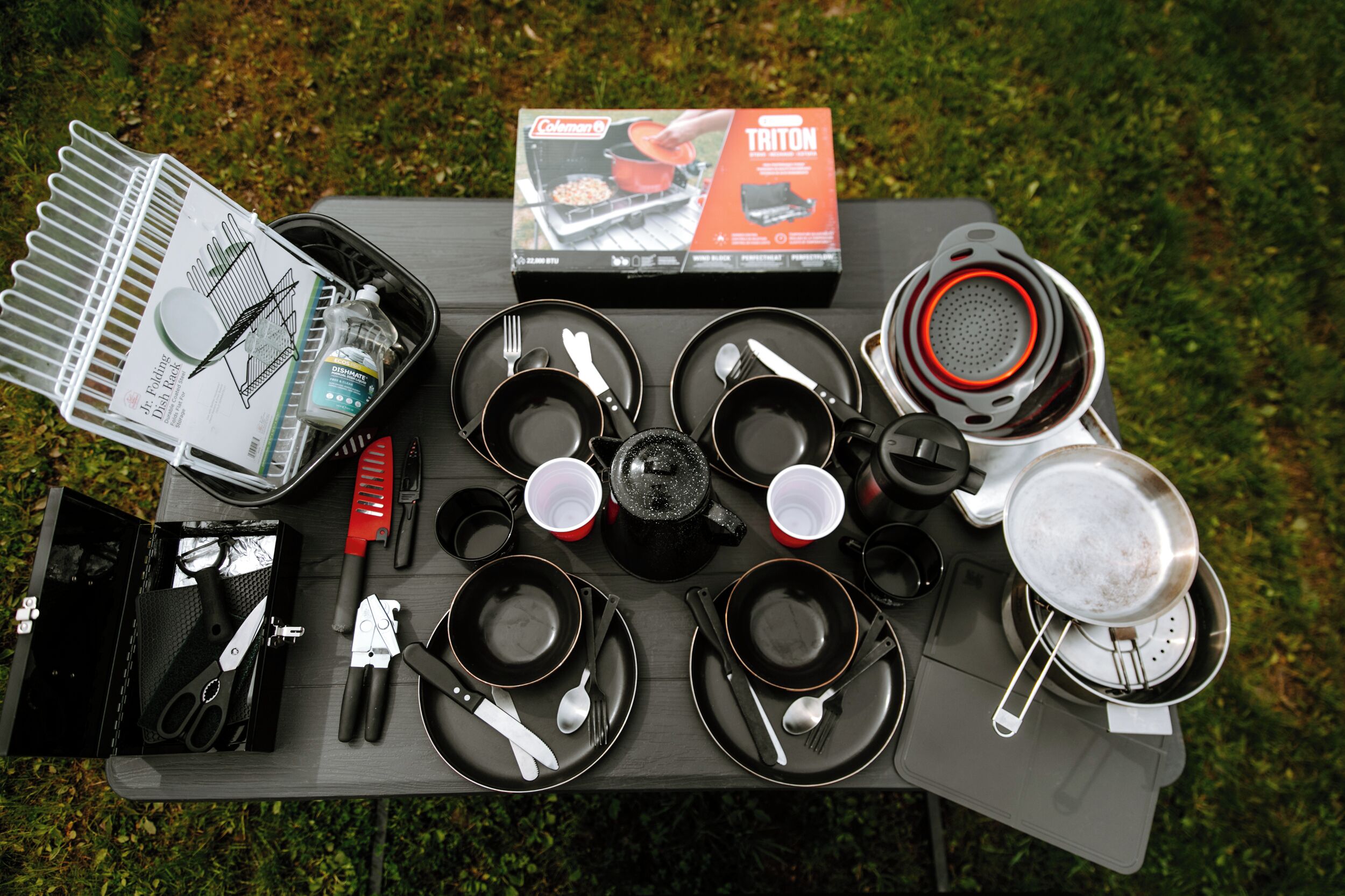 A camping setup with a portable grill, cooking utensils, and a table set for a meal.