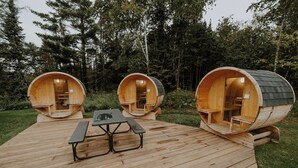 Three wooden barrel-style cabins with a picnic table in between, set on a wooden deck in a forested area. - North Shore Camping Co. (Beaver Bay)