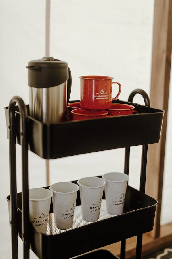 A black metal cart with a coffee pot, red cups, and white cups with logos. - North Shore Camping Co. (Beaver Bay)