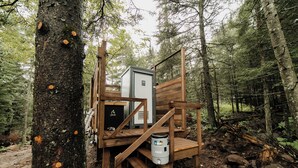 A wooden cabin with a small staircase leading to a platform with a water container and a metal box. - North Shore Camping Co. (Beaver Bay)