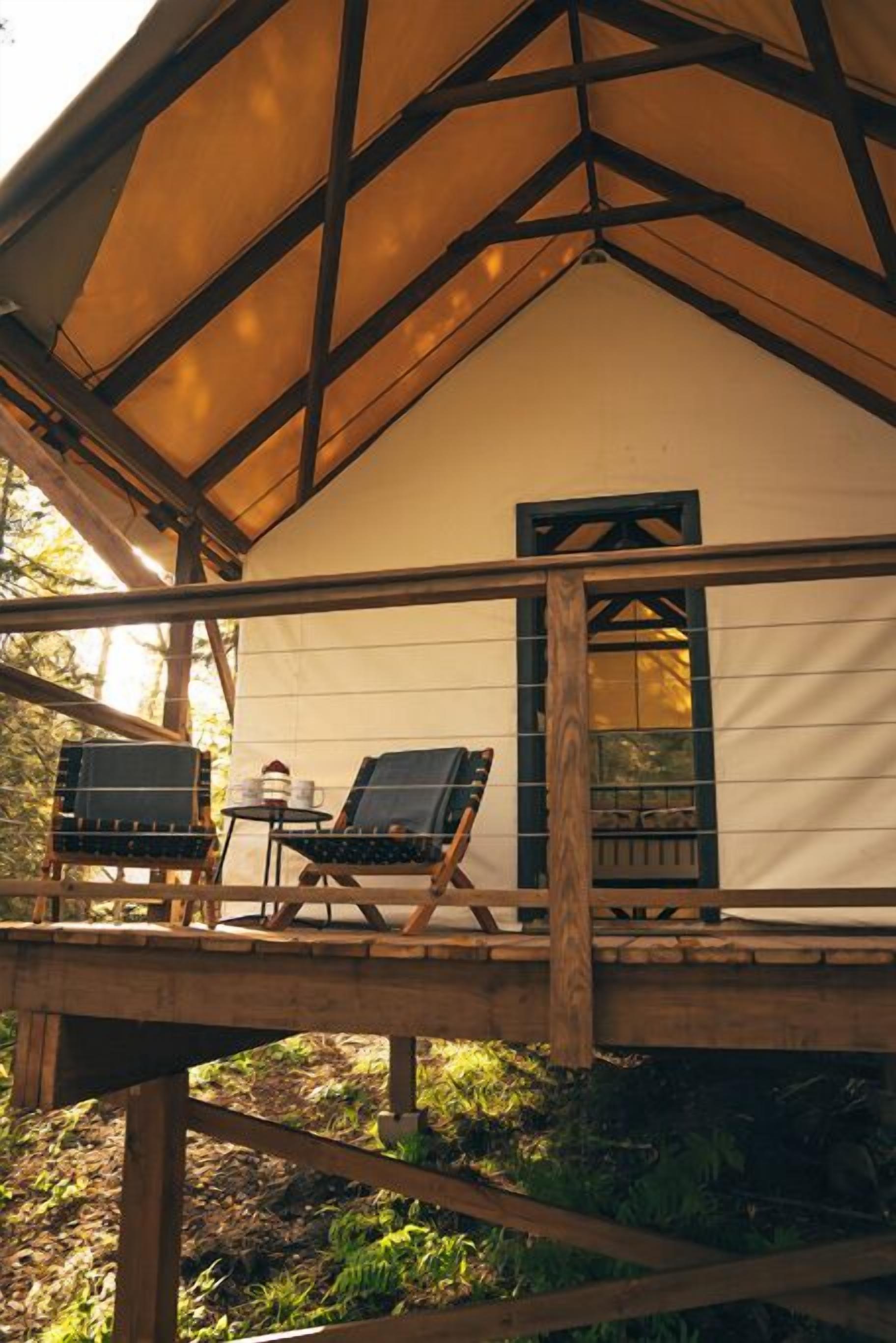 A wooden deck with two lounge chairs and a small table, under a large canopy.