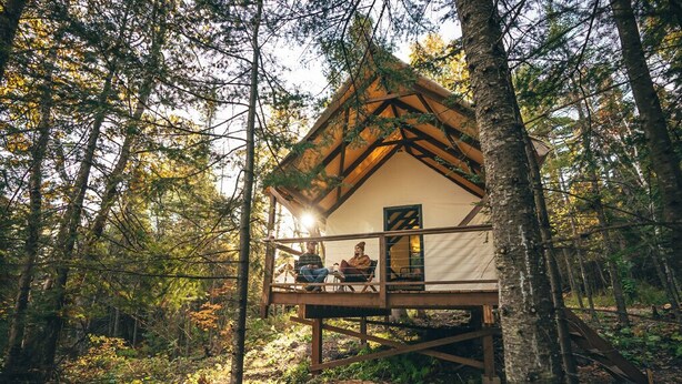 A cabin in a forest with a wooden deck and a small porch. - North Shore Camping Co. (Beaver Bay)