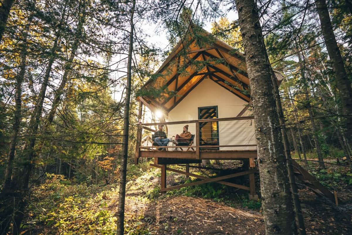 A cabin in a forest with a wooden deck and a small porch.
