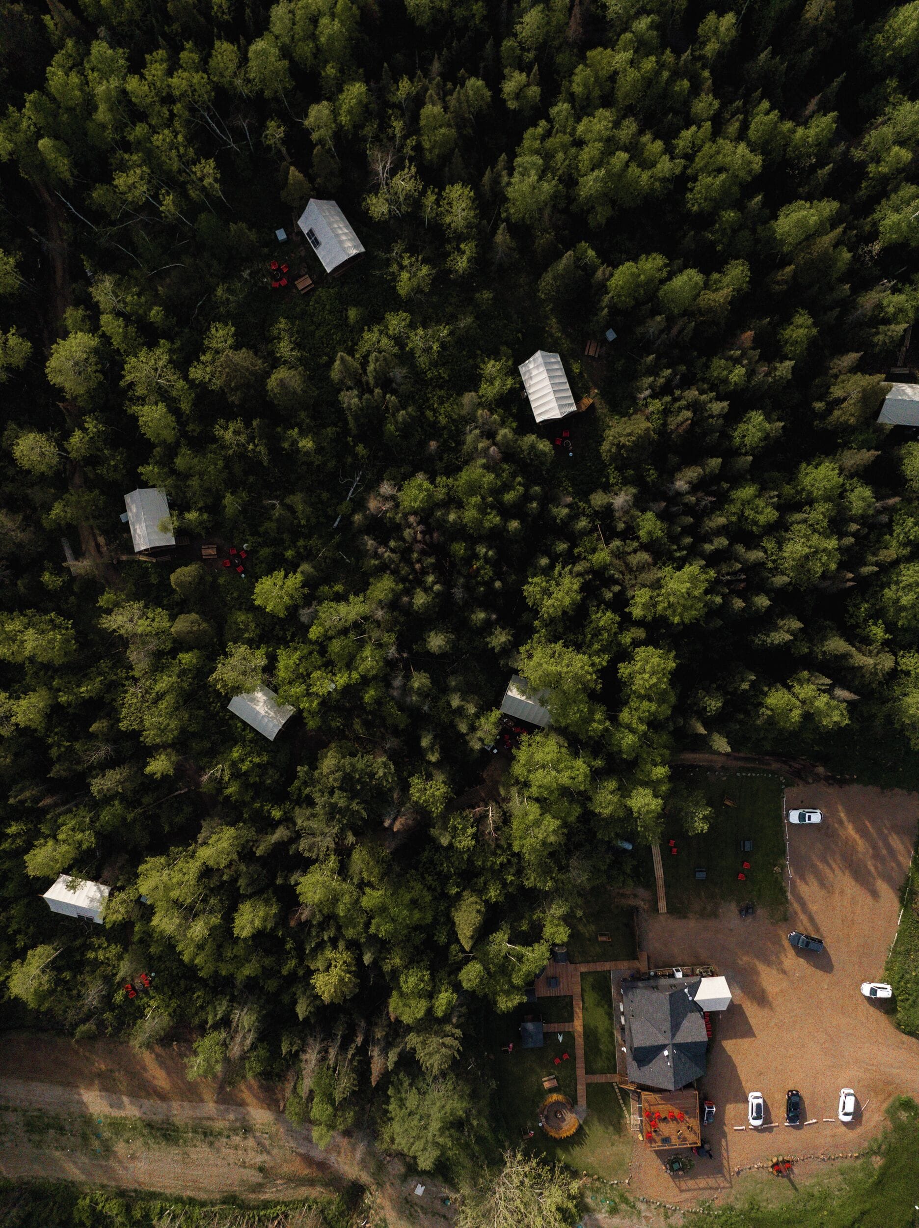 Vista aérea de una zona boscosa con varias cabañas y un pequeño aparcamiento.