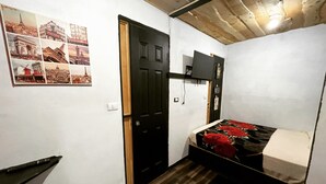 A small, compact room with a bed, a desk, and a wall-mounted TV. - Poas Volcano Rooms  (Sabanilla)
